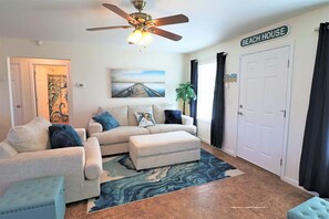 A living room with a sofa set, a ceiling fan, a rug, and a painting. - SANDY BEACH HOUSE IS 600 STEPS TO BEACH! SINGLE LEVEL HOME IN GREAT LOCATION! (Mexico Beach)
