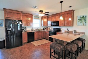 Una cocina con armarios de madera, un refrigerador negro, un microondas y una isla central con taburetes de bar.