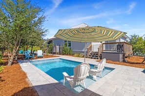 Ein Schwimmbad mit zwei weißen Stühlen, einer überdachten Terrasse und einem Haus mit einer Veranda.