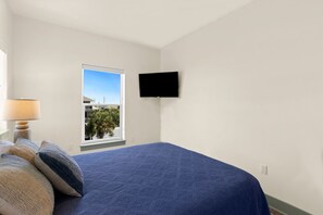 Un dormitorio con cama, ventana, televisor y lámpara.