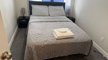 A neatly made bed with a patterned bedspread and pillows, a folded towel on the bed, and a nightstand with a lamp beside it.