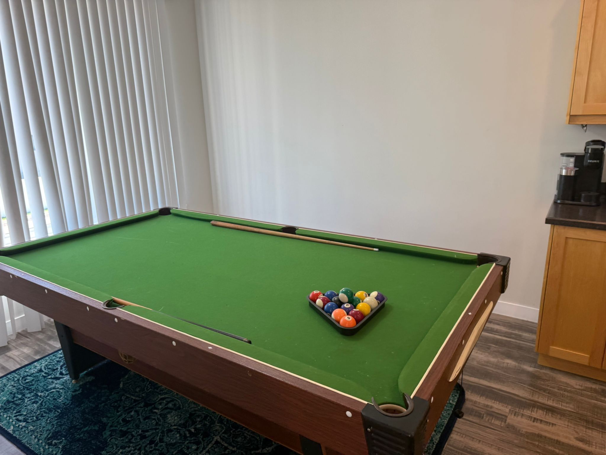 Une table de billard avec un jeu de billes au centre, un tapis vert et un cadre en bois.