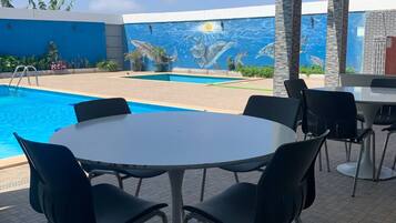 Un espace extérieur abrité avec une piscine, une table ronde entourée de chaises et une fresque représentant la vie marine sur le mur.