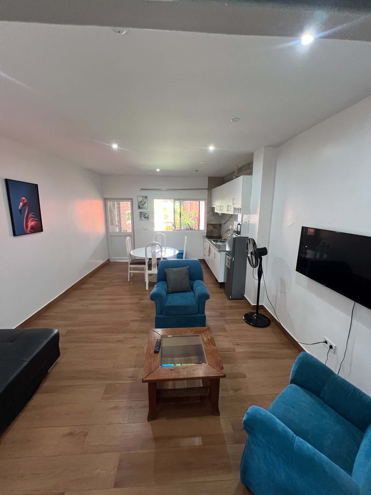A spacious living area with a blue sofa, a coffee table, and a television mounted on the wall.