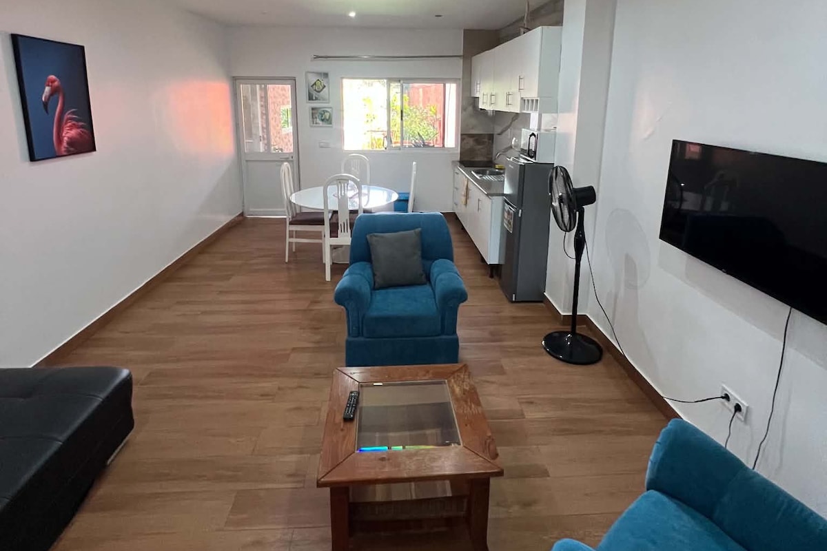 Amplia sala de estar con un sofá azul, una mesa de centro y un televisor instalado en la pared.