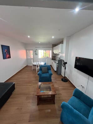 Amplia sala de estar con un sofá azul, una mesa de centro y un televisor instalado en la pared.