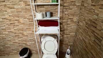 Une petite salle de bain avec des toilettes, une étagère contenant des articles de toilette et un balai.