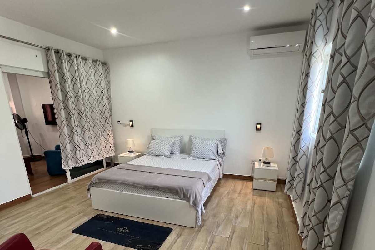 A bedroom with a bed, bedside tables, a red chair, a floor lamp, and patterned curtains.