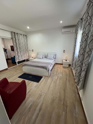 A bedroom with a bed, bedside tables, a red chair, a floor lamp, and patterned curtains.