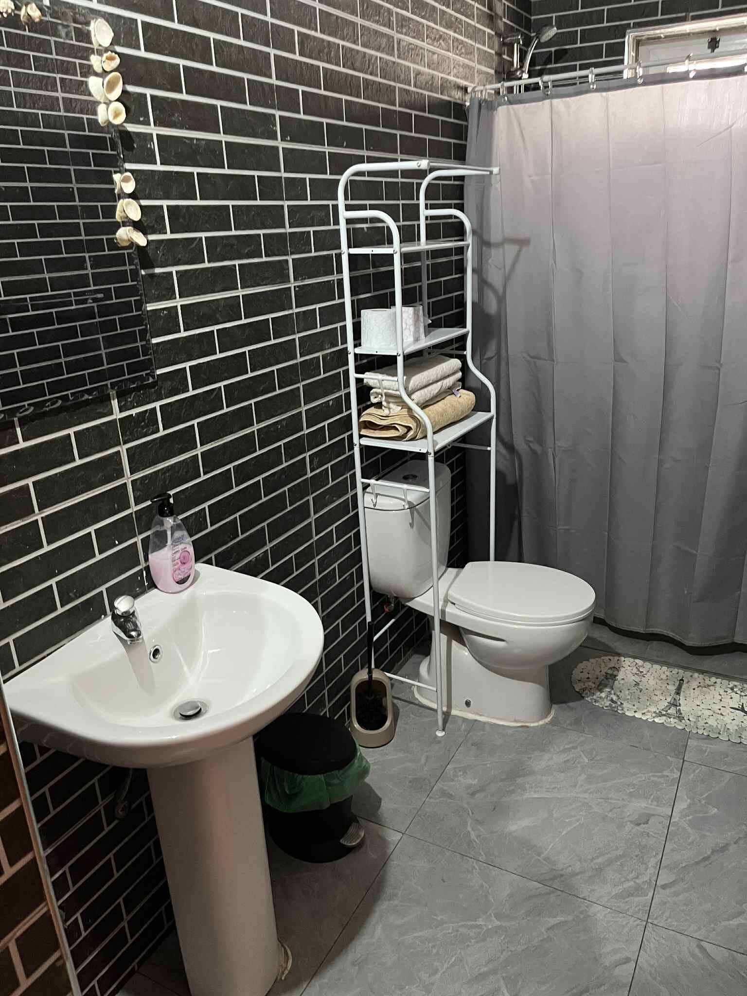A bathroom with a white sink, toilet, and a metal shelf unit with towels.