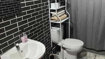 A bathroom with a white sink, toilet, and a metal shelf unit with towels.