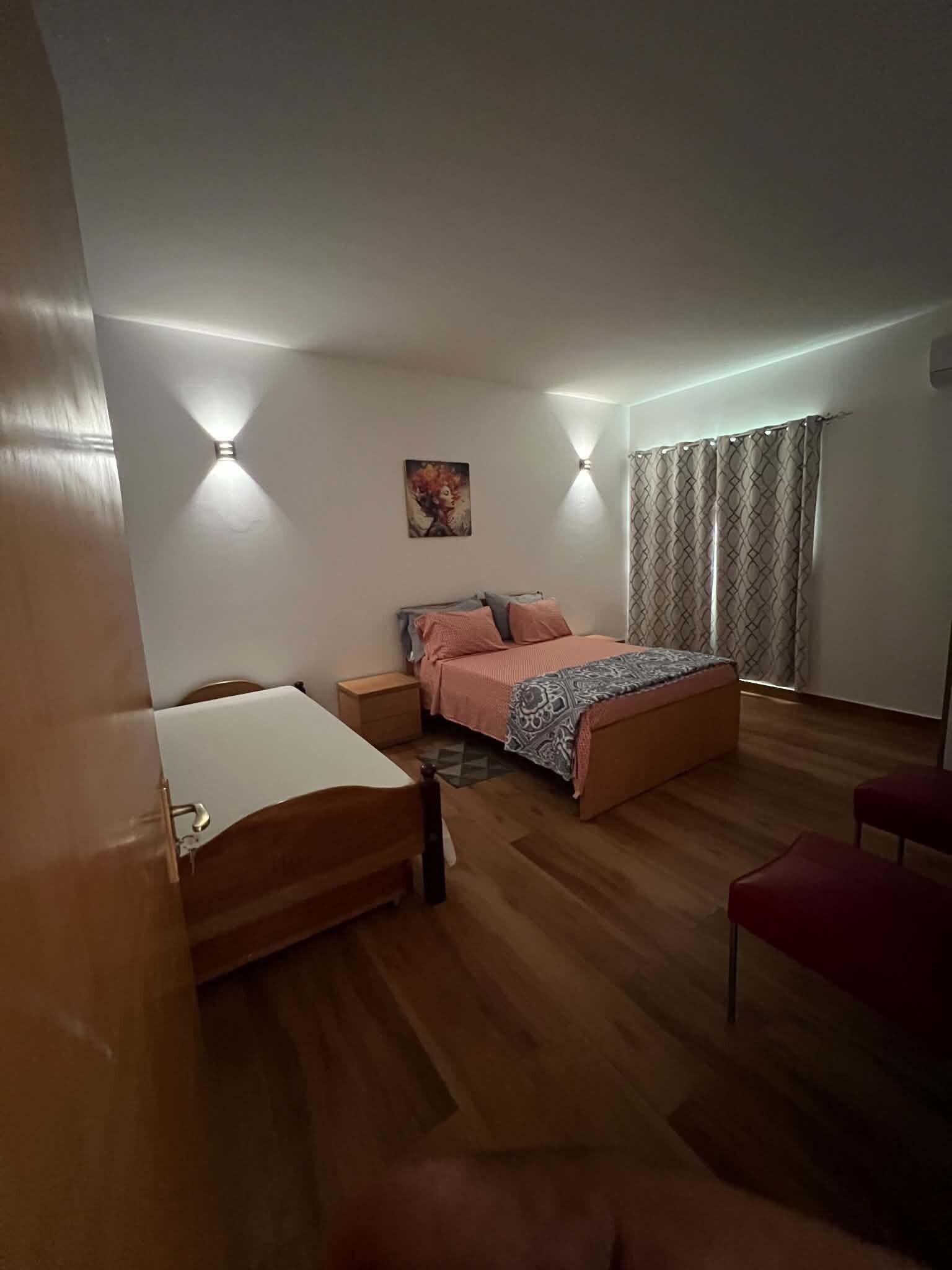 Een slaapkamer met een bed, nachtkastjes, een bureau, een stoel en een raam met gordijnen.