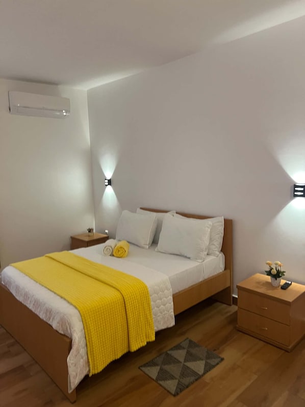 Un dormitorio con cama, mesitas de noche y aire acondicionado de pared.
