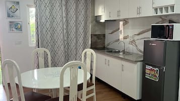 Une cuisine moderne avec des armoires blanches, un four à micro-ondes encastré et un coin repas comprenant une table et des chaises blanches.