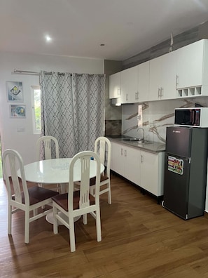 Una cocina moderna con armarios blancos, microondas integrado y comedor con mesa y sillas blancas.
