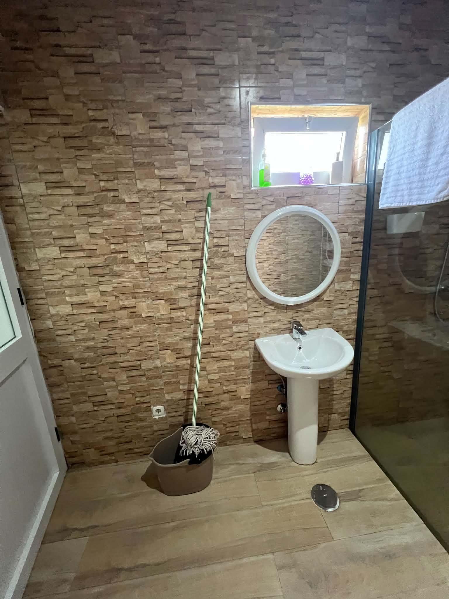 A bathroom with a stone wall, a sink, a mirror, and a mop.