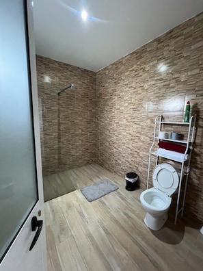 Un baño moderno con ducha, inodoro y un estante con artículos de tocador.