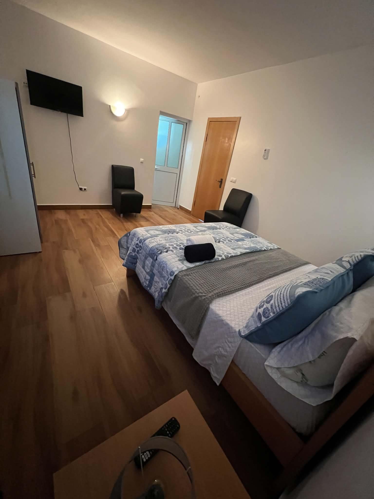 A bedroom with a bed, a desk, a chair, a TV, and a door.