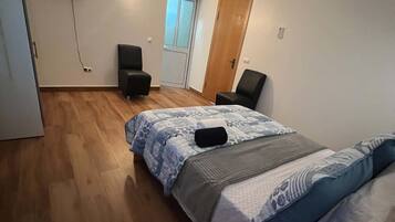 A bedroom with a bed, a desk, a chair, a TV, and a door.