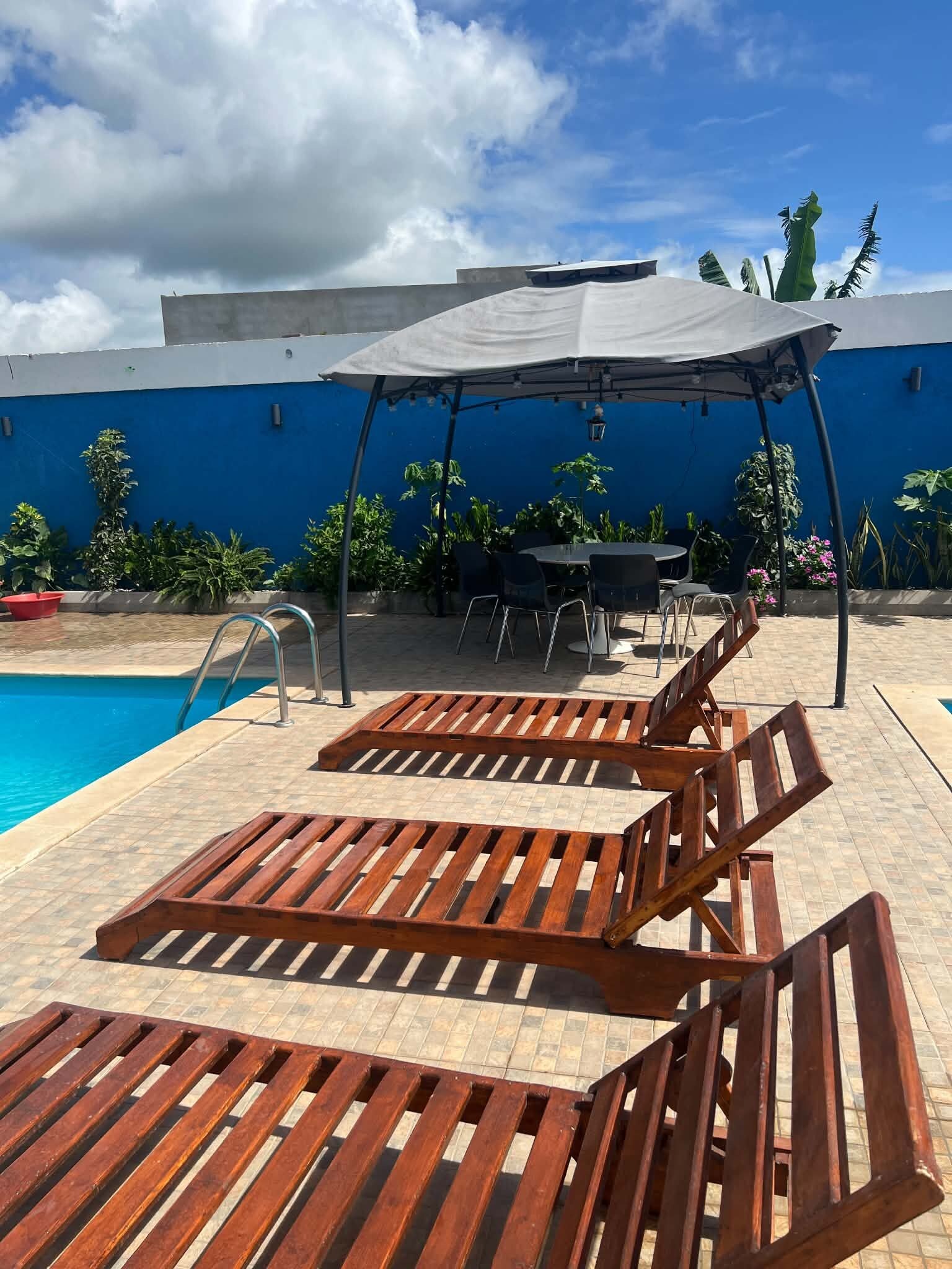 Ein Poolbereich mit Holzliegen, einer überdachten Sitzgelegenheit und einer blauen Wand.