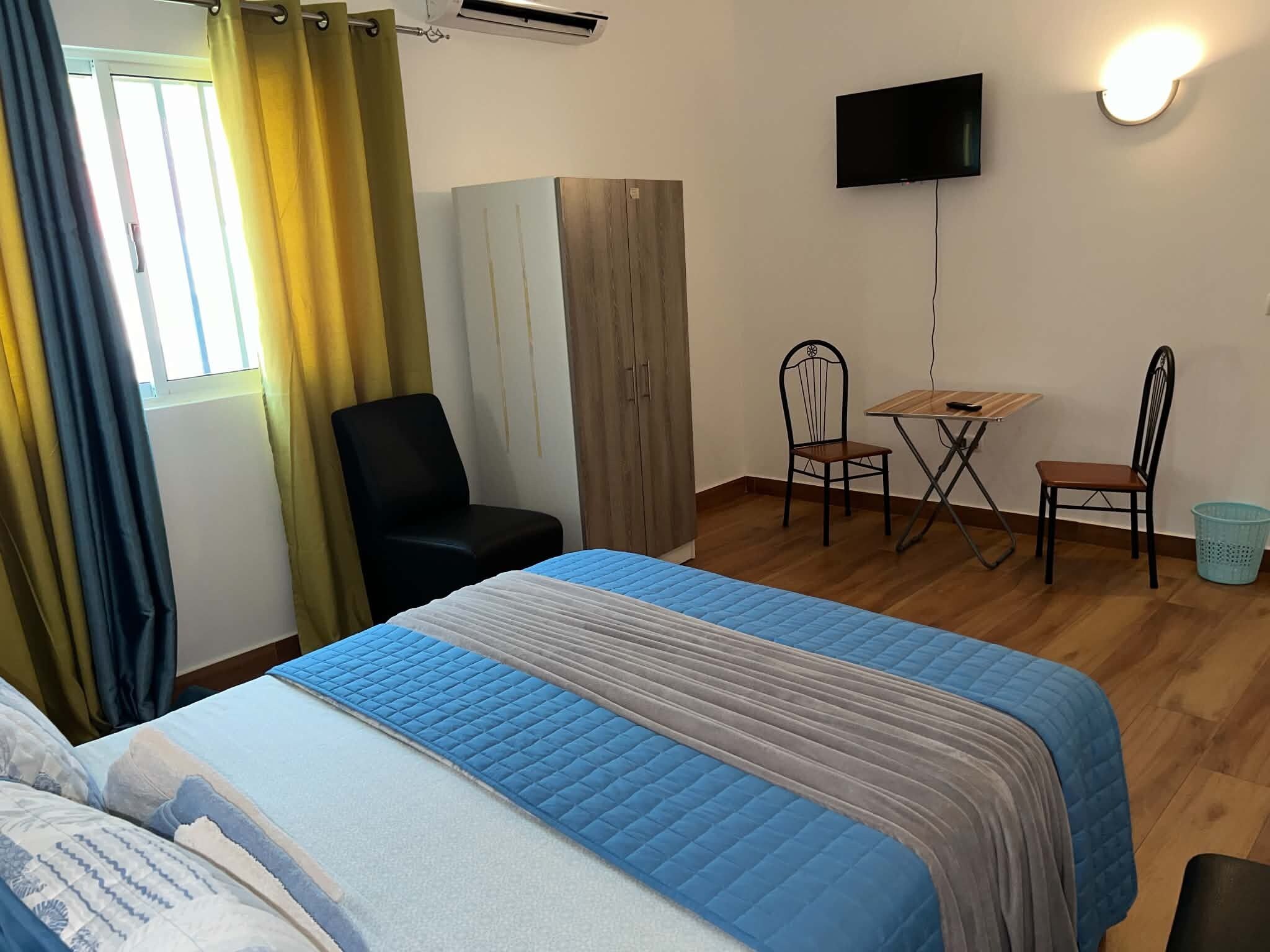 Habitación de hotel con cama, escritorio, dos sillas, televisor y ventana con cortinas.