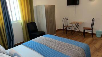 Habitación de hotel con cama, escritorio, dos sillas, televisor y ventana con cortinas.