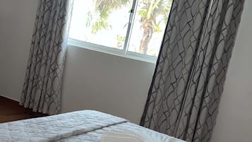 A bedroom with a bed, curtains, and a window with a view of palm trees.