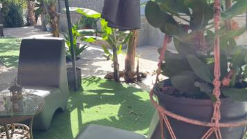 Un espace extérieur aménagé avec une table et des chaises, entouré de plantes en pot et agrémenté d’un pot suspendu en macramé.