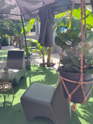 Zona d'estar a l'exterior amb una taula i cadires, envoltada de plantes en testos i un penjador de macramé.