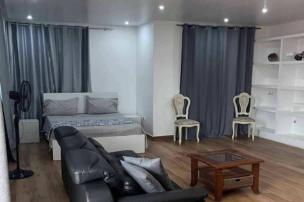 Un dormitorio moderno con cama, sofá, dos sillones, una mesita y un ventilador.
