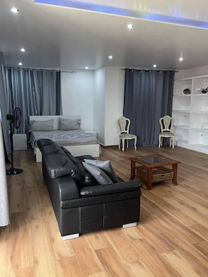 Un dormitorio moderno con cama, sofá, dos sillones, una mesita y un ventilador.