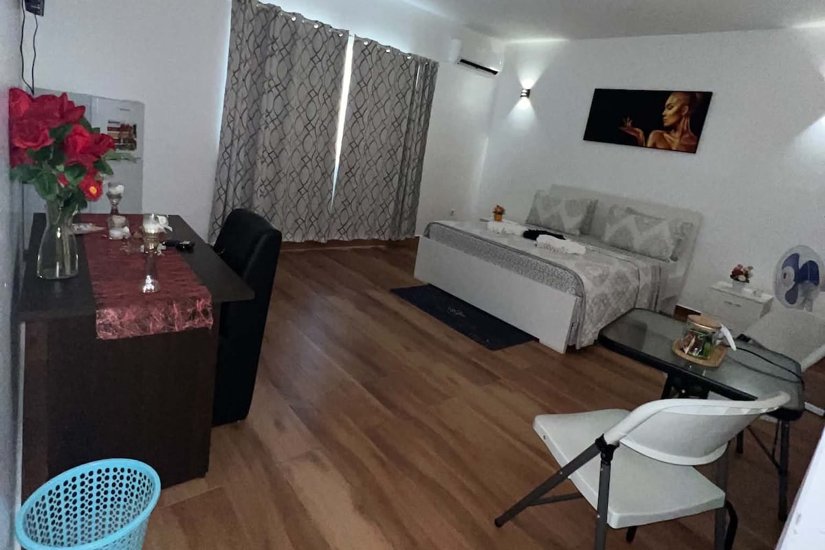 Un espacio habitable compacto con sofá, una mesa de comedor, un televisor montado en la pared y una mesita con un jarrón de flores.