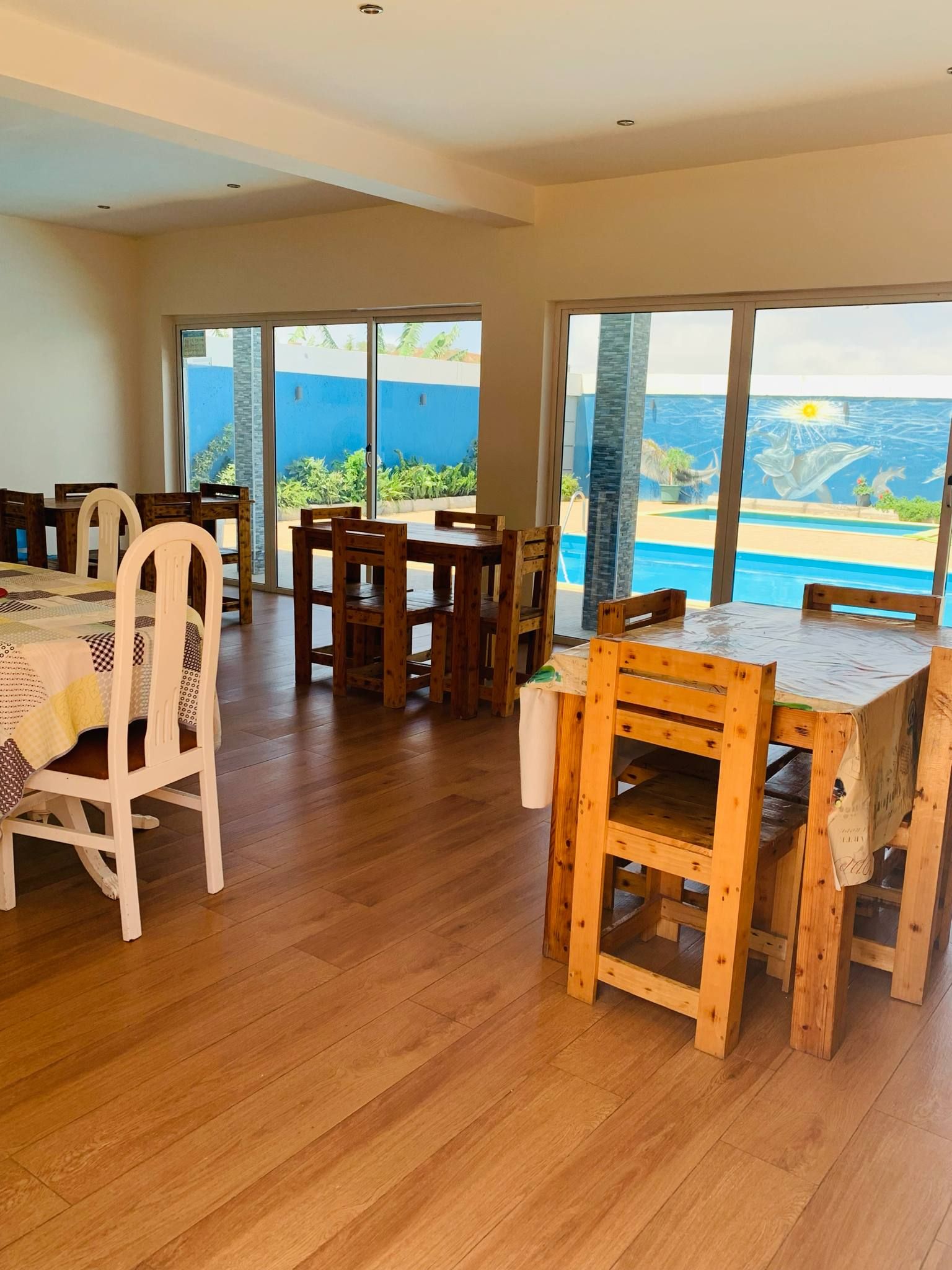 Un comedor con mesas y sillas de madera, ventanas amplias con vista al mar y piso de madera.