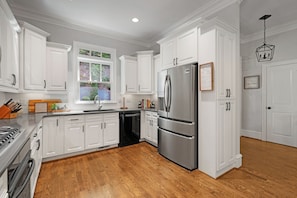 A kitchen with white cabinetry, a stainless steel refrigerator, a dishwasher, and a wooden floor. - Whitetail Ridge Hideaway - Big Canoe, GA (Big Canoe)