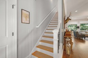 A staircase with wooden steps and white walls, leading to a living area with a sofa and decorative items. - Whitetail Ridge Hideaway - Big Canoe, GA (Big Canoe)