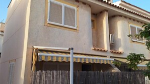A two-story building with a flat roof, a balcony with a striped awning, and a white fence with a spherical finial. - Holiday Home 'Relaxing Cozy House' with Mountain View, Shared Pool and Wi-Fi (Santa Pola)