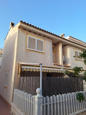 A two-story building with a flat roof, a balcony with a striped awning, and a white fence with a spherical finial. - Holiday Home 'Relaxing Cozy House' with Mountain View, Shared Pool and Wi-Fi (Santa Pola)