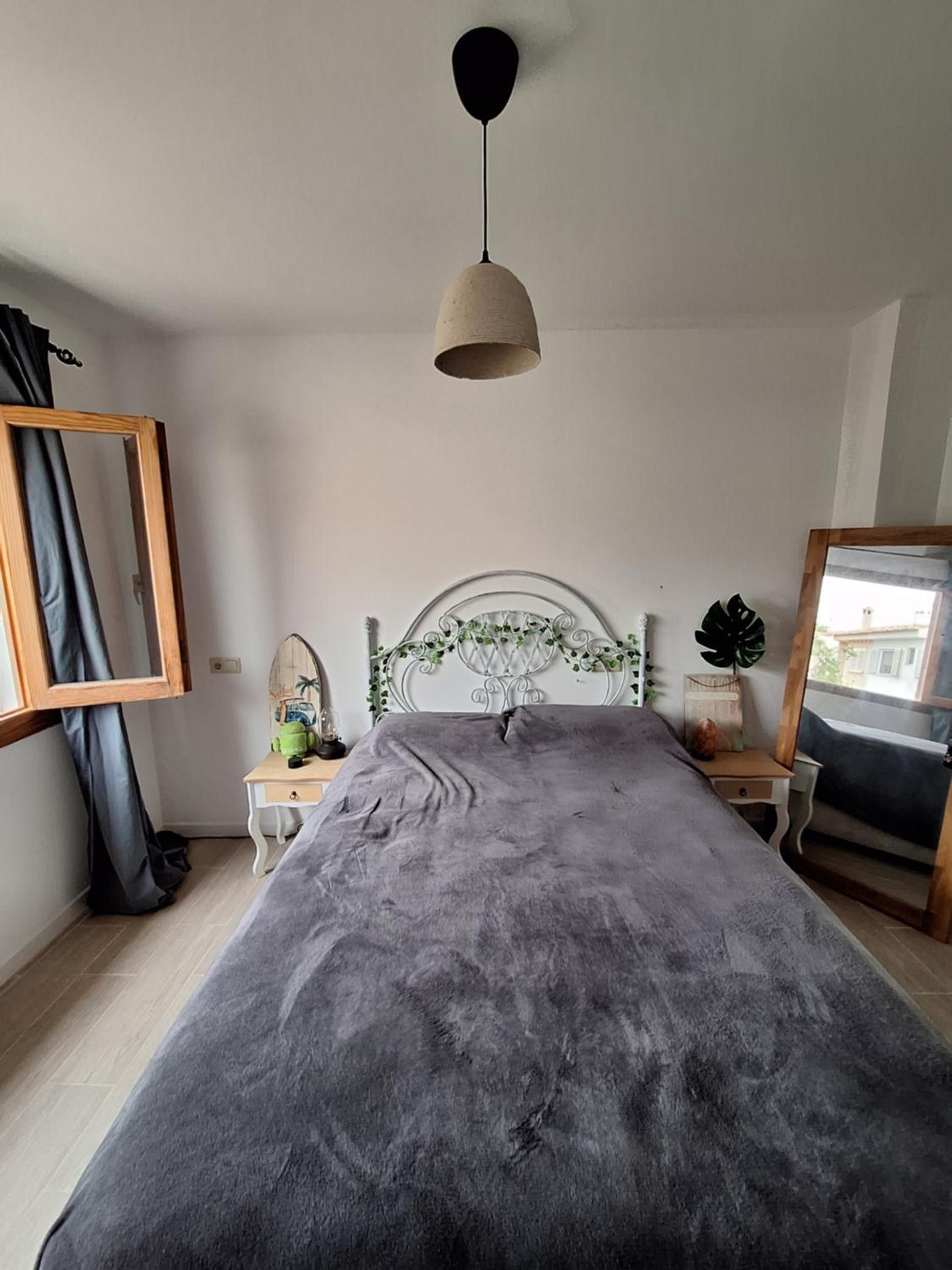 A bedroom with a bed, a bedside table, a mirror, and a hanging light fixture.