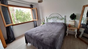 A bedroom with a bed, a window with curtains, a bedside table with a lamp, and a mirror. - Holiday Home 'Relaxing Cozy House' with Mountain View, Shared Pool and Wi-Fi (Santa Pola)