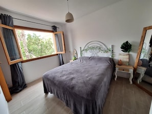 A bedroom with a bed, a window with curtains, a bedside table with a lamp, and a mirror. - Holiday Home 'Relaxing Cozy House' with Mountain View, Shared Pool and Wi-Fi (Santa Pola)