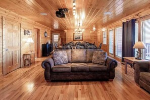 A log cabin interior with a central seating area, wooden floors, and a chandelier. - Stylish 8BR Cabin - Hot tub & Views - Sevierville (Sevierville)