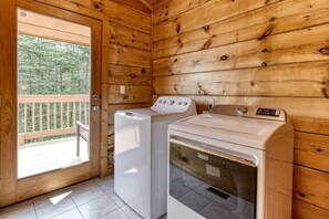 A laundry room with two washing machines, wooden walls, and a door leading to an outdoor deck. - Inviting 3BR Cabin - Hot tub & Fireplace - Smokies (Sevierville)