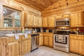 A kitchen with wooden cabinets, stainless steel appliances, and a window overlooking greenery. - Inviting 3BR Cabin - Hot tub & Fireplace - Smokies (Sevierville)