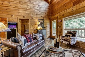A cabin interior with a leather sofa, a plaid-patterned armchair, a small round table, and a television. - Inviting 3BR Cabin - Hot tub & Fireplace - Smokies (Sevierville)