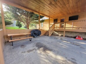 Un espace extérieur abrité comprenant un banc en bois, un barbecue et un escalier menant à un niveau supérieur.