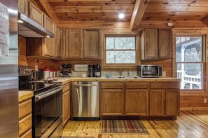 A kitchen with wooden cabinets, stainless steel appliances, and a large window. - Serene 4BR Cabin - Hot tub & Game Room - Townsend (Townsend)