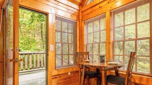 A wooden cabin interior with a dining table and chairs, large windows with blinds, and a door leading outside. - Serene 1BR Cabin - Hot tub & Fireplace - Smokies (Sevierville)