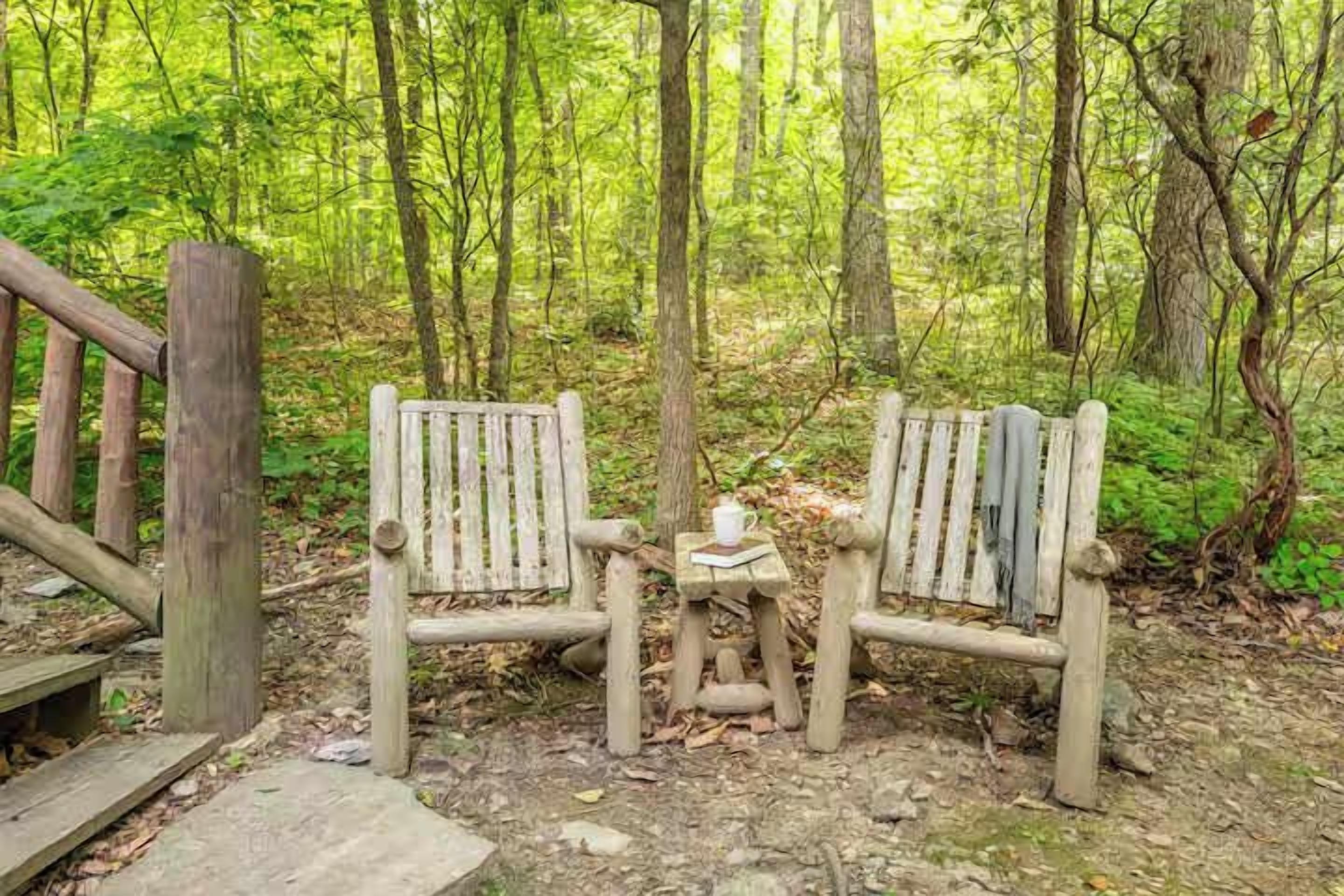 Zwei Holzstühle und ein kleiner Tisch in einer Waldlandschaft.