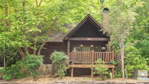 A cabin with a wooden deck, surrounded by trees. - Serene 1BR Cabin - Hot tub & Fireplace - Smokies (Sevierville)