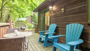 An outdoor wooden deck with a table and chairs, a grill, and a wooden cabin with a green door. - Serene 1BR Cabin - Hot tub & Fireplace - Smokies (Sevierville)